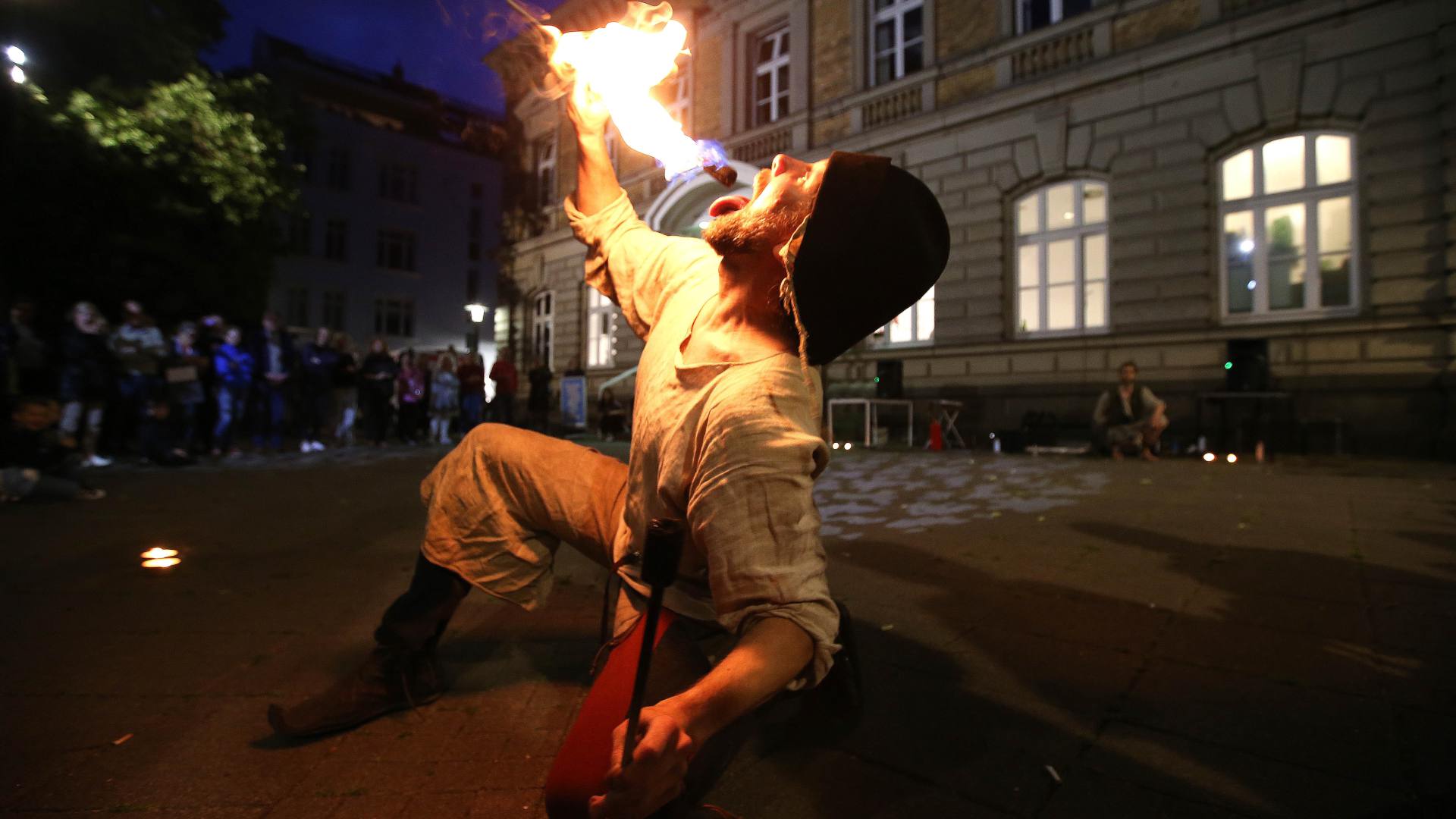 A fire-eater in ancient clothing kneels in front of the Alte Post, holding a flaming torch in front of his mouth